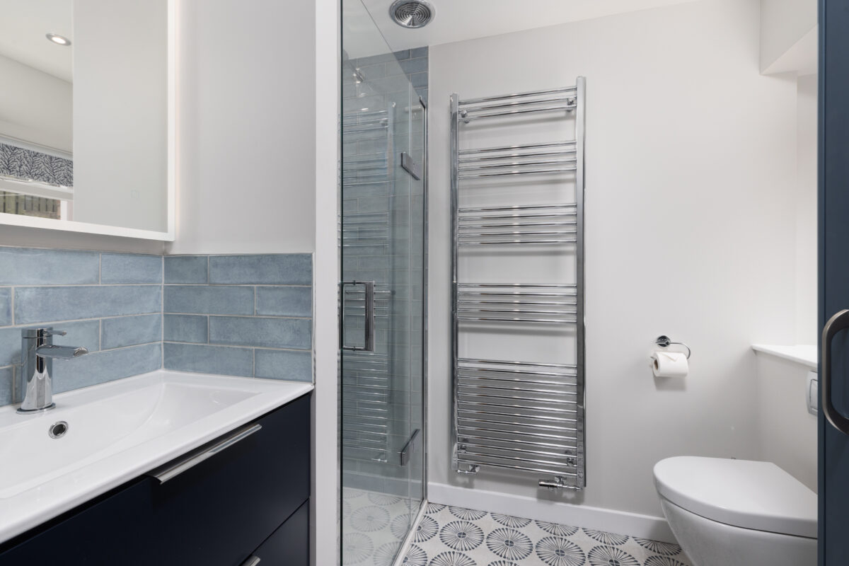A modern shower room remodel incorporating a dedicated shower area, a large chrome radiator, a vanity unit, and a WC.